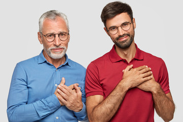 Horizontal shot of satisfied two men of different age, make gratitude gesture, feel thankful to...