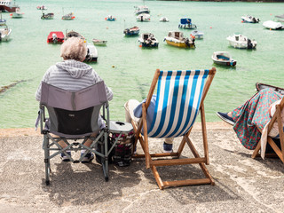 OAP couple sitting in deckchairs, enjoying the sun, in St Ives harbour, Cornwall, England.