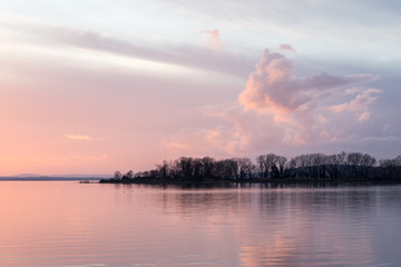 A shoot of a sunset over a lake, with beautiful warm colors and clouds and trees reflections on water