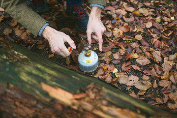 Male hands setup and operate canister stove. Hiking in the autumn forest with backpacking stove
