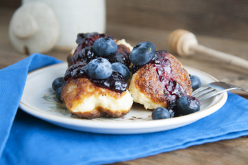 Homemade cheese donuts with berry jam and blueberry. Healthy breakfast or snack, round plate, rustic wooden background.