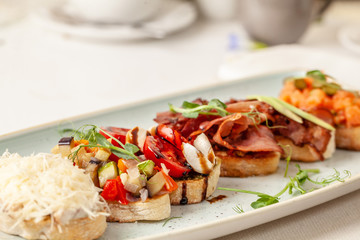 The concept of Italian cuisine, a tourist breakfast in a restaurant. different bruschetta on a long plate with a mug of coffee. Copy space, selective focus