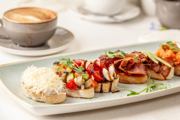 The concept of Italian cuisine, a tourist breakfast in a restaurant. different bruschetta on a long plate with a mug of coffee. Copy space, selective focus