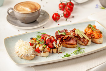 The concept of Italian cuisine, a tourist breakfast in a restaurant. different bruschetta on a long plate with a mug of coffee. Copy space, selective focus