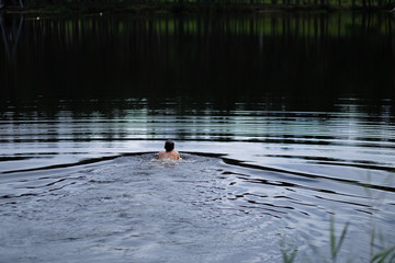 A young man sails on the surface of a forest lake in the early morning