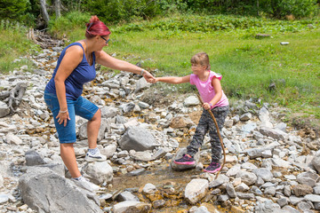 Mum helps her daughter to cross a mountain stream