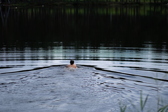 A young man sails on the surface of a forest lake in the early morning