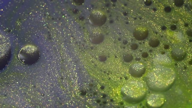 Gold liquid glittery paint bubbles. Abstract background. Macro. Motion mixed colorful ink