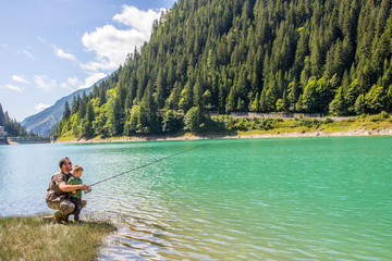 happy father and son fishing together on a mountain lake