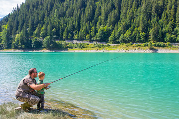 happy father and son fishing together on a mountain lake