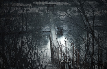 Creepy dark old suspension bridge across the river in the fog. Background for halloween