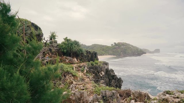 Woman walking on cliff with trees and shrubs at white sandy beach in Central Java, Indonesia