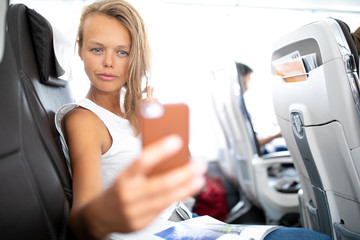 Young happy woman making selfie photo with passport document sitting on the aircraft seat near a...