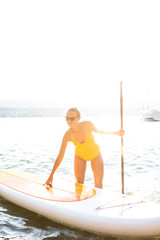 SUP Stand up paddle board concept - Pretty, young woman paddle boarding on a lovely lake in warm late afternoon light