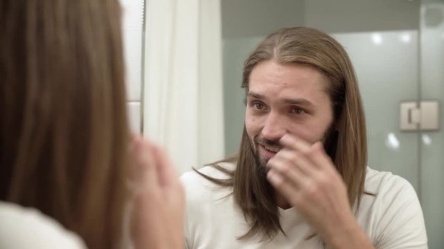 Man At Bathroom Looking In Mirror And Touching Face