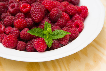 Red and delicious raspberries with mint in a white bowl