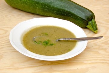 Delicious green zucchini soup with zucchini on a wooden table with a spoon and soup bowl