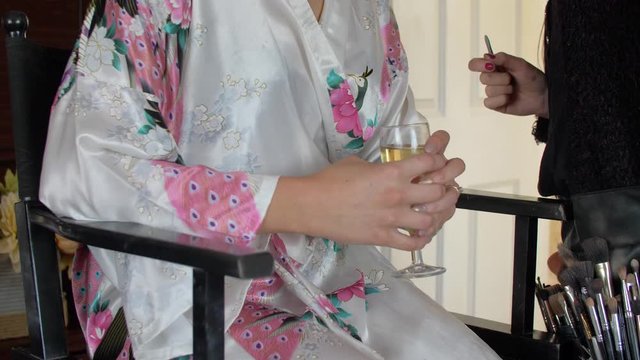 girl in rope holding glass with champagne while makeup artist doing makeup
