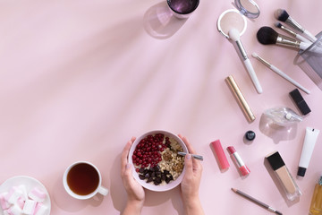 Female workspace with coffee cup, oat flakes, make up and cosmetics set, on pastel pink desk with shadow, top view and flat lay. Fashion pink woman workplace for blogging. Beautiful morning breakfast.