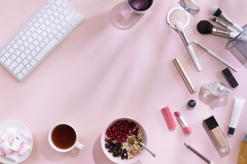 Female workspace with computer, coffee cup, oat flakes, make up and cosmetics set, on pastel pink desk with shadow, top view and flat lay. Fashion pink woman workplace. Beautiful morning breakfast.