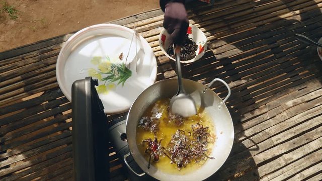 Woman turning over deep frying tarantulas inside a wok using a metal spatula (upper view)
