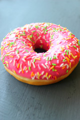 Pink donut with multi-colored sprinkles on a black background, top view