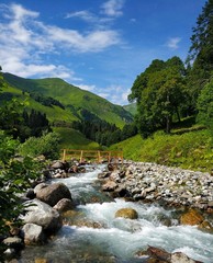 A mountain river with a bridge with green mountains and blue sky in the background