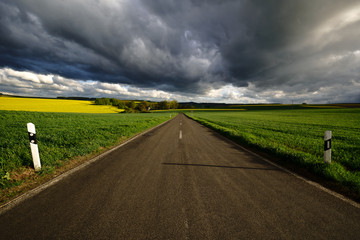 Empty road in the countryside, large dark clouds, sunset light.