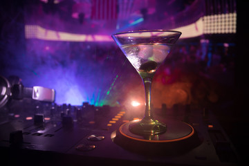 Glass with martini with olive inside on dj controller in night club. Dj Console with club drink at...