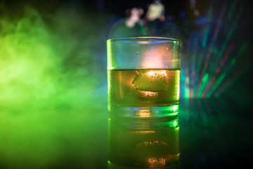 selective focus pure whisky with ice cube inside whisky glass on dark foggy background alcohol drink concept.