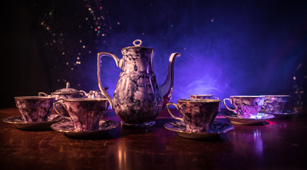 Food background tea and coffee theme. Old vintage ceramic tea or coffee pot with cups jug and sugar cup on dark background with lights and smoke. Silhouettes of ceramic tea pot and cup.