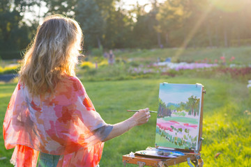The painter paints oil paintings in the garden at sunset
