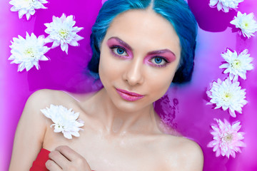 Portrait of young woman female girl adult / fashion luxury model with colorful blue hair relaxing in bathtub with flowers and pink water. Organic skin care, beauty and body care concept. Partial nude