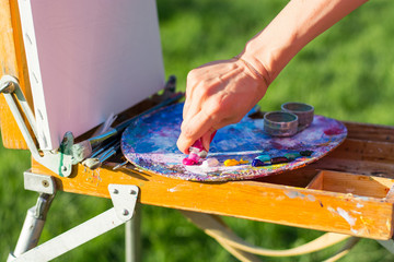 The artist's hand, which squeezes the oil paint from the tube into the palette on the easel
