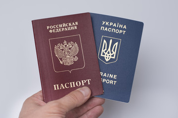 Ukrainian and Russian international passports in the man's hand. White background. Close up