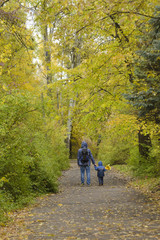 Obraz premium Father and son on their shoulders walk through the autumn park. Back view