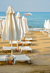 Sandy beach with white umbrellas and sun loungers in the summer at dawn