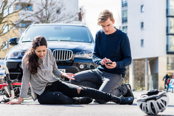 Full length view of a worried young driver calling the ambulance after hitting and injuring accidentally a female bicyclist on a city street  © Kzenon
