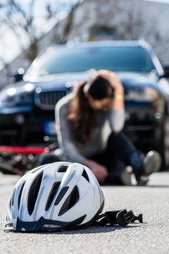Bicycling helmet on the asphalt after accidental collision between the bicycle of a sorrowful young woman and a 4x4 car in the city