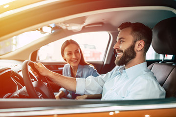 Happy young smiling couple riding in car on the road. Handsome bearded man is sitting at the wheel.