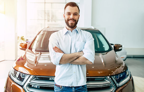 Happy handsome bearded man with crossed arms while buying a car in dealership