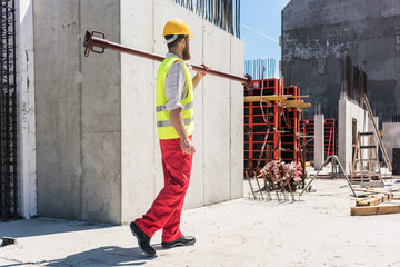 Full length of a blue-collar worker wearing safety equipment, while carrying a heavy metallic bar...