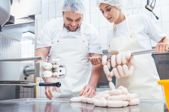 Team of butchers, woman and man, filling sausage in meat industry