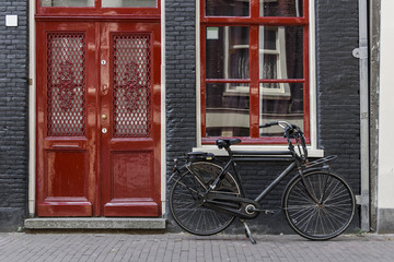 Fototapeta na wymiar A single bicycle outside a red door in Amsterdam, Netherlands