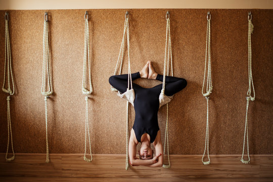 pleasant gifted gymnast is doing bound angle pose upside down on the ropes. a new kind of yoga. full length photo
