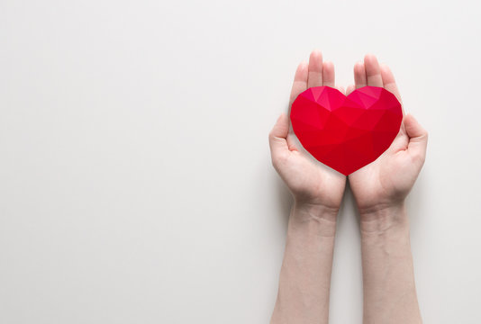 Red polygonal heart in female hands on white background. Symbol of charity and donation. Place for text.