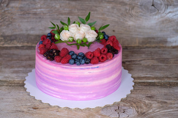 beautiful home cake with pink and purple cream, decorated with white roses and berries of BlackBerry, blueberries, raspberries