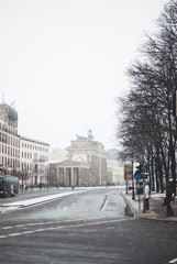 Winter cityscape of Berlin covered with snow. Snowflakes flying against over the street behind Brandenburg Gate