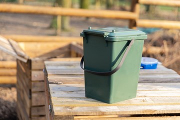 Green bucket bin on wooden compost heap 