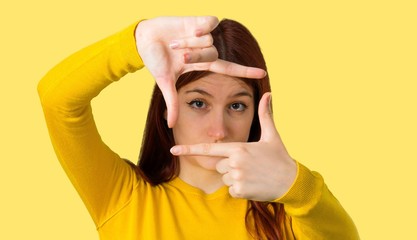 Young redhead girl with yellow sweater focusing face. Framing symbol on isolated yellow background